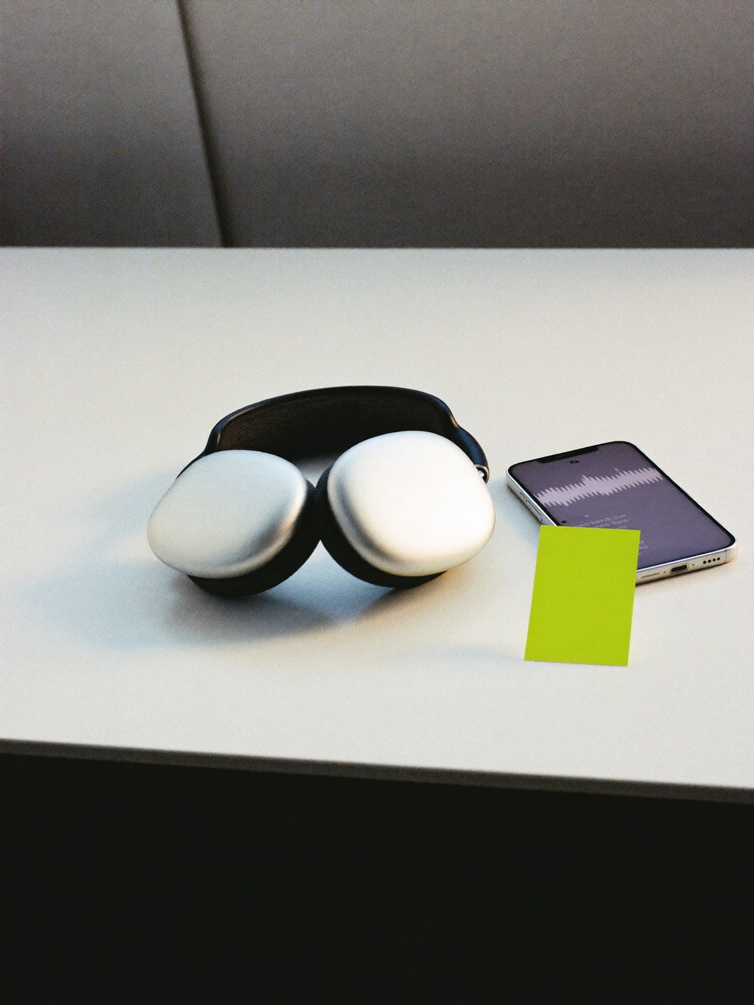 Silver headphones and a phone showing a waveform on a clean white surface.